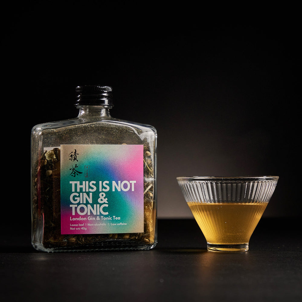A bottle of Gin & Tonic Tea by MoreTea alongside a cup with tea leaves visible, on a dark background.